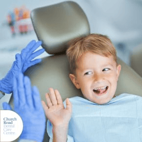 A young boy on a chair at the dentist high fiving an adult's hand with a blue glove