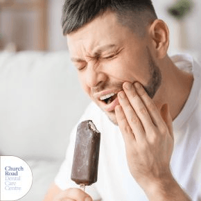 A man eating an ice lolly, holding his mouth and grimacing.