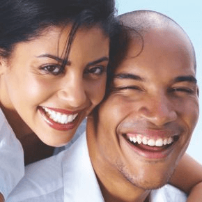 A happy couple smile at the camera, showing off their healthy teeth.